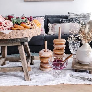 Living room picnic with donut stacks, and rustic wood table piled with yummy treats, and dried florals on floor.