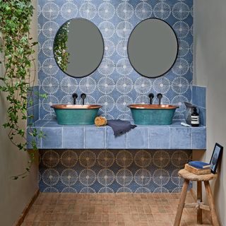 Twin basins on a blue tiled countertop with patterned blue wall tiles and matching wall mirrors