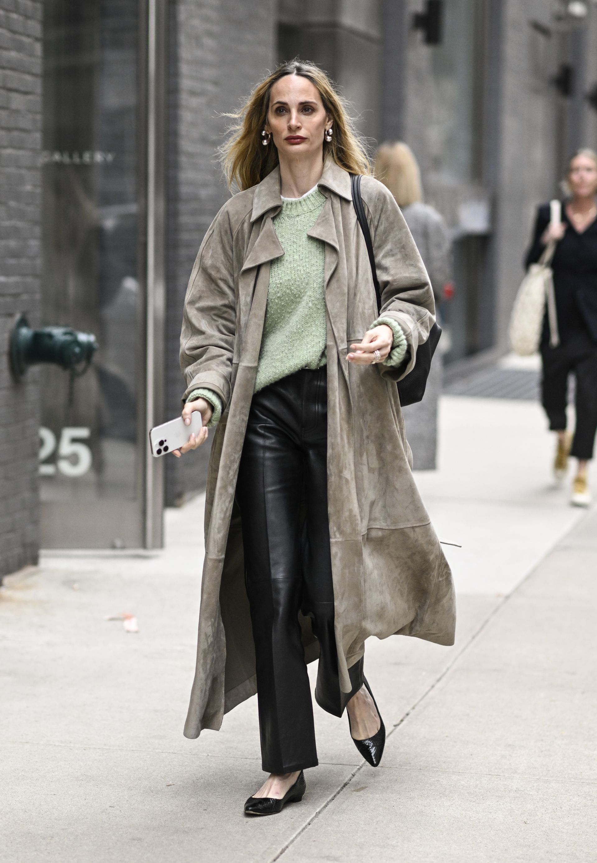 A woman wears a suede jacket, t-shirt, black leather pants, flats