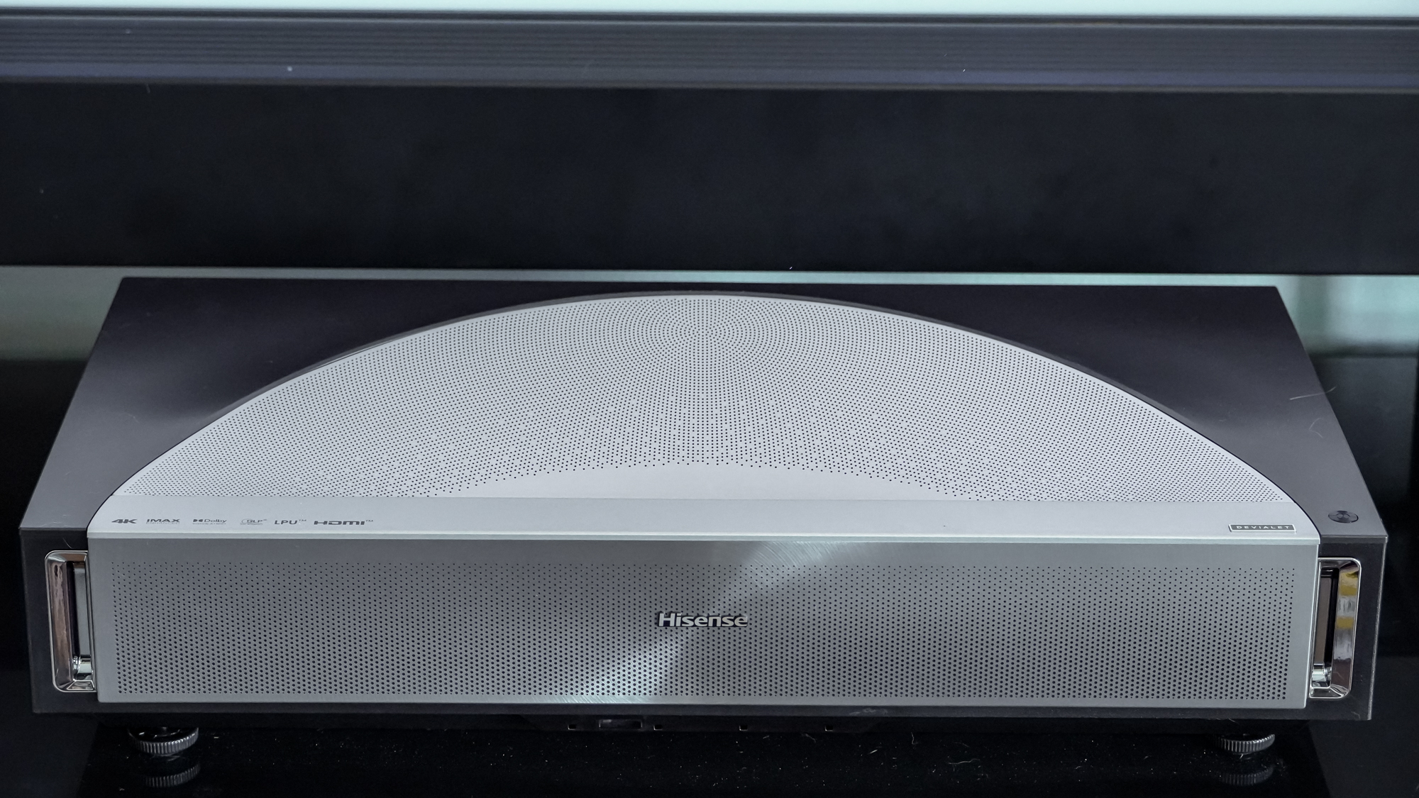 A Hisense PX4 Pro projector on a home media center shelf