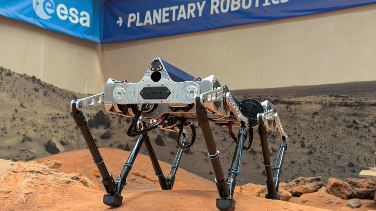 A four legged robot stands on a reddish brownish surface