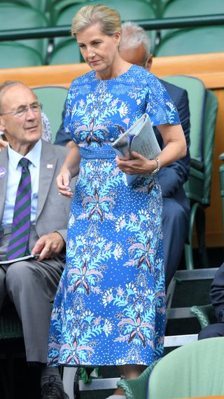 Duchess Sophie wears a blue floral dress and carries a slogan clutch bag as she attends day nine of the Wimbledon Tennis Championships in 2019
