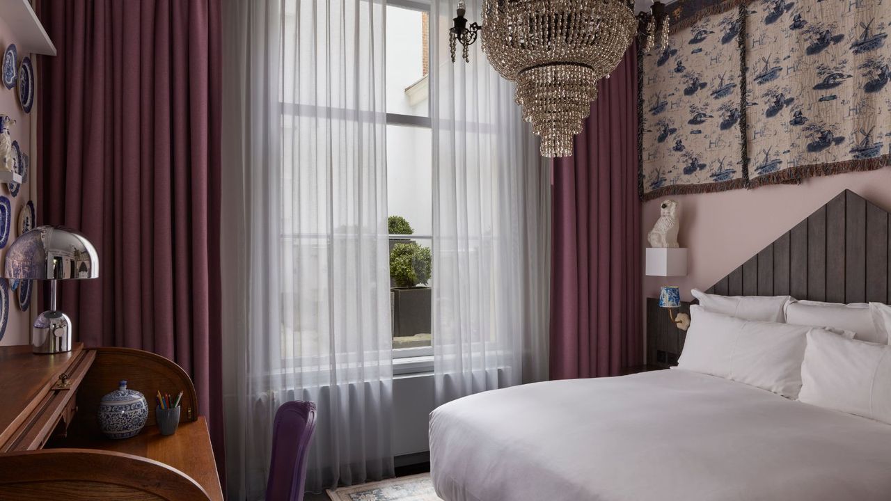 hotel bedroom with a lilac and pink color scheme decorated with vintage tapestry wall hangings above the bed and a large crystal chandelier