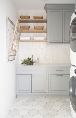 A small laundry room with a fold-out drying rack and pale green/gray cabinets