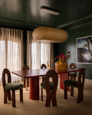 Dining room with dark green walls, red table and sculptural wood chairs