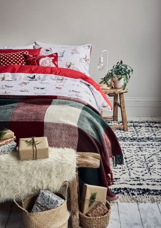 A bedroom with red, cream and grey check throw, Berber-style cream and black rug, red and white Christmas themed bedding and faux fur throw with woven baskets at end of bed