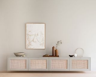 Gray sideboard with rattan panels, wooden flooring, gray-beige painted walls, sideboard decorated with vases and ornaments, one piece of artwork mounted above
