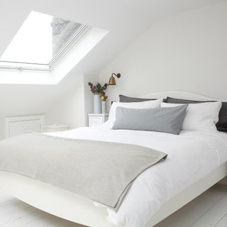 bedroom with wooden flooring white bed with pillows and white walls