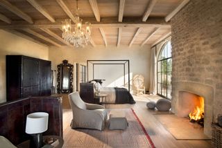 Minimalist bedroom with natural wood floors and ceilings, stone fireplace, black framed fourposter bed