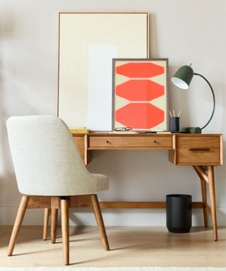 A wooden desk with orange wall art and a white office chair next to it
