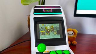 Sega Astro City Mini arcade machine on woodgrain desk with Golden Axe: The Revenge of Death Adder on screen.