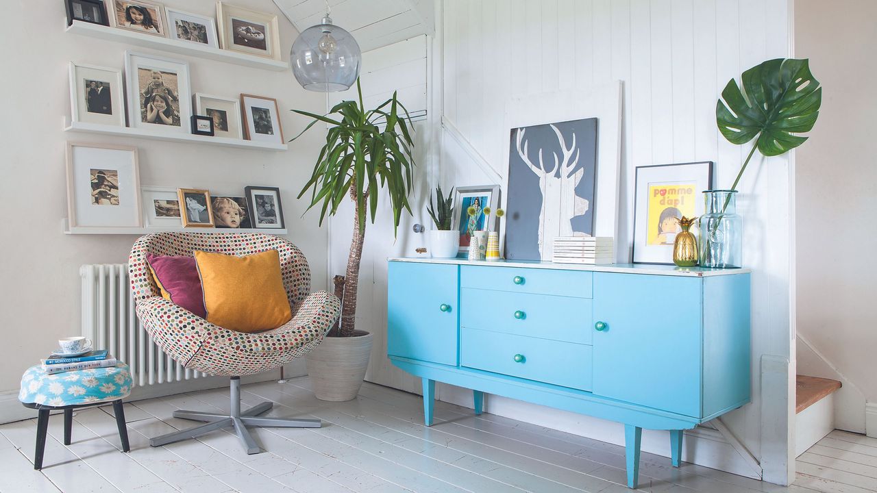 Hallway with painted floorboards, blue sideboard, white shelves displaying framed photographs, armchair and footstool. Gill and Sandro Deriu&#039;s renovated three bedroom detached cottage in Cork, Ireland.