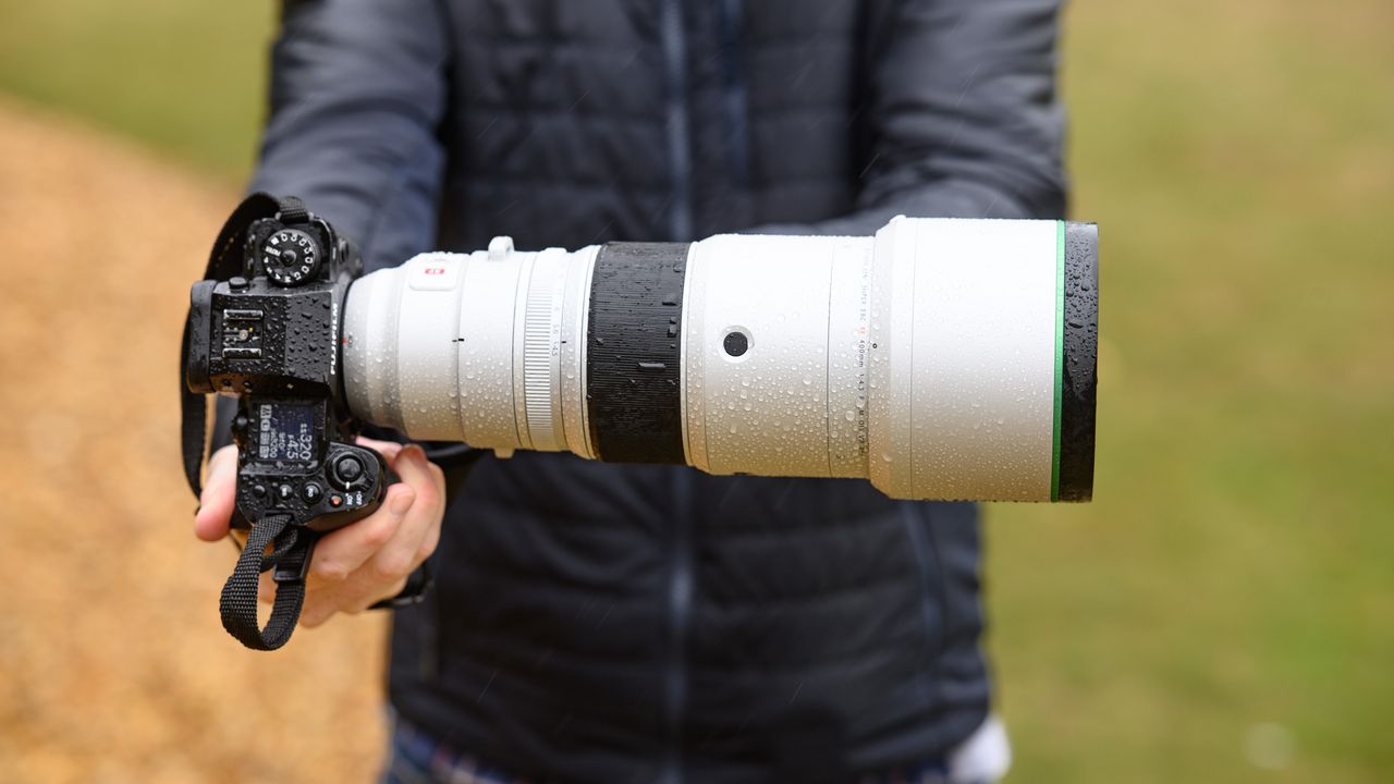 TechRadar Cameras Editor Tim Coleman holding the Fujifilm XF 400mm F4.5 R LM OIS WR telephoto prime lens attached to a Fujifilm X-H2S camera, out in the rain taking pictures