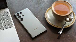 Samsung Galaxy S23 Ultra posé sur de face sur une table a côté d'un ordinateur portable et d'un thé