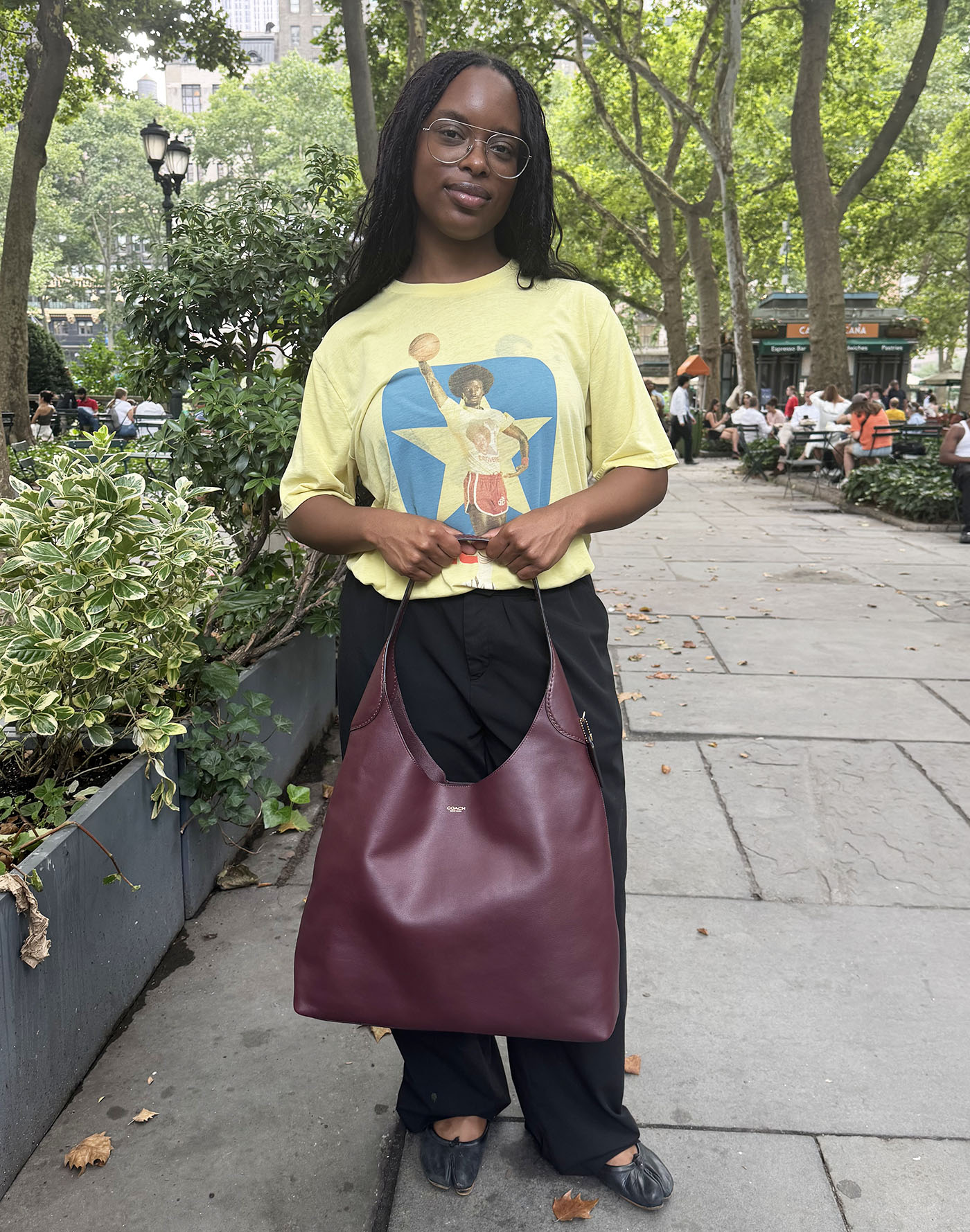 A woman wearing a yellow T-shirt, black pants, and a Coach burgundy Brooklyn Shoulder Bag