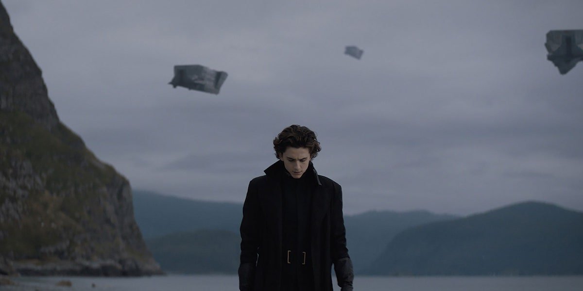 Paul Atreides (Timothee Chalamet) wears a long black coat as he walks on a beach in 2020&#039;s Dune