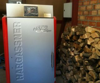 A red and silver biomass boiler in a plant room with logs stacked up beside it