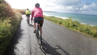 Image shows tow cyclists on a Cornish coastal road