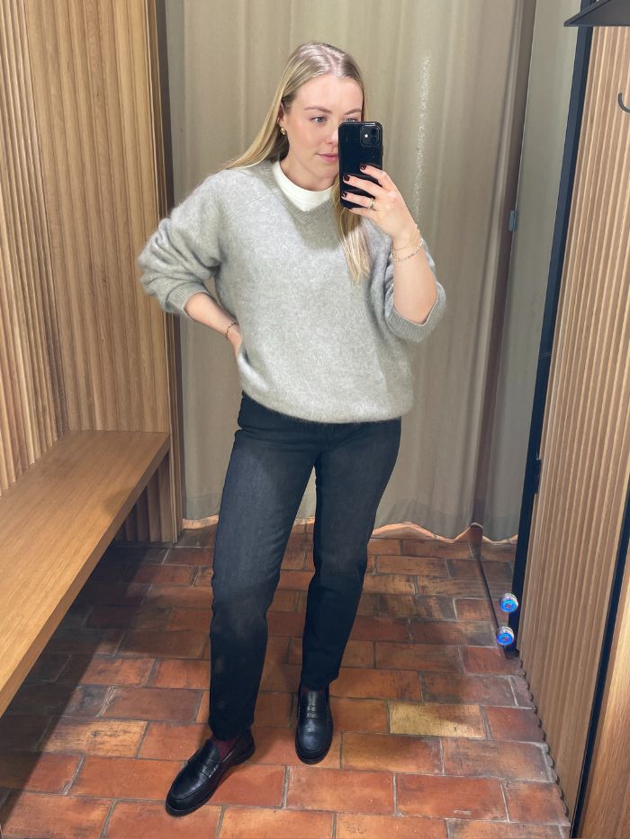 Woman wears grey jumper, black jeans and black loafers