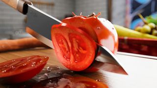 Someone cuts a tomato on a chopping board