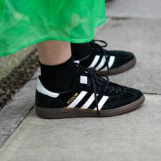  A guest wears a green short puffy sleeves / long midi dress, black socks, black suede with white leather logo sneakers from Adidas, outside 16Arlington, during London Fashion Week February 2023 on February 18, 2023 in London, England