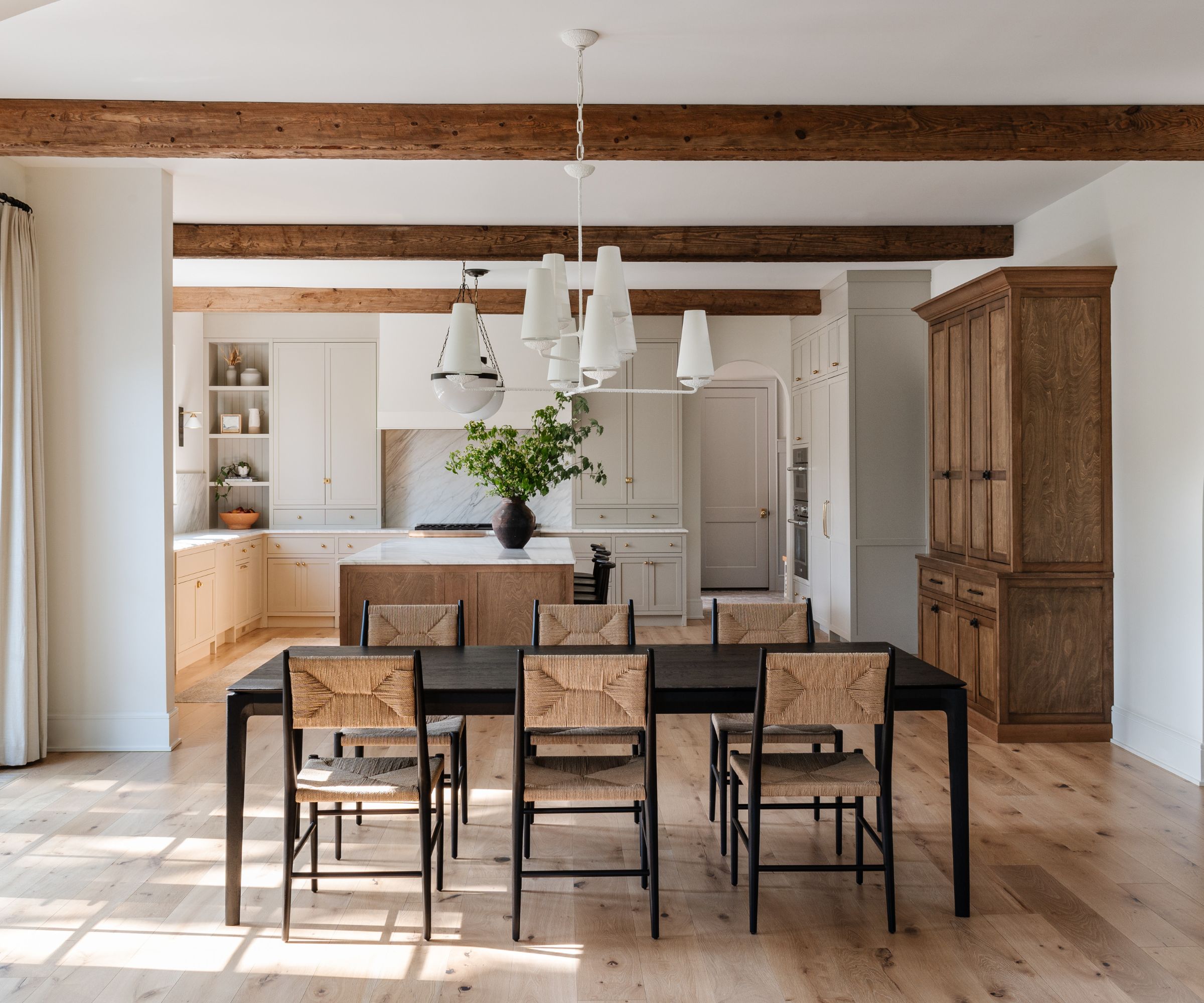 A large open-plan kitchen with white cabinets, a wooden island, and an adjoining dining area with a large black table