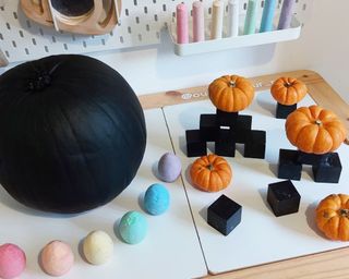 A pumpkin painted with two coats of black chalk paint alongside egg-shaped pastel chalks in a playroom setting
