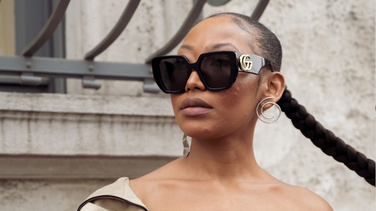 A guest wears beige pants, beige top and a jacket, white shoes, black bag and sunglasses outside the Prada show during the Milan Fashion Week Womenswear Fall/Winter 2023/2024 on February 23, 2023 in Milan, Italy. 