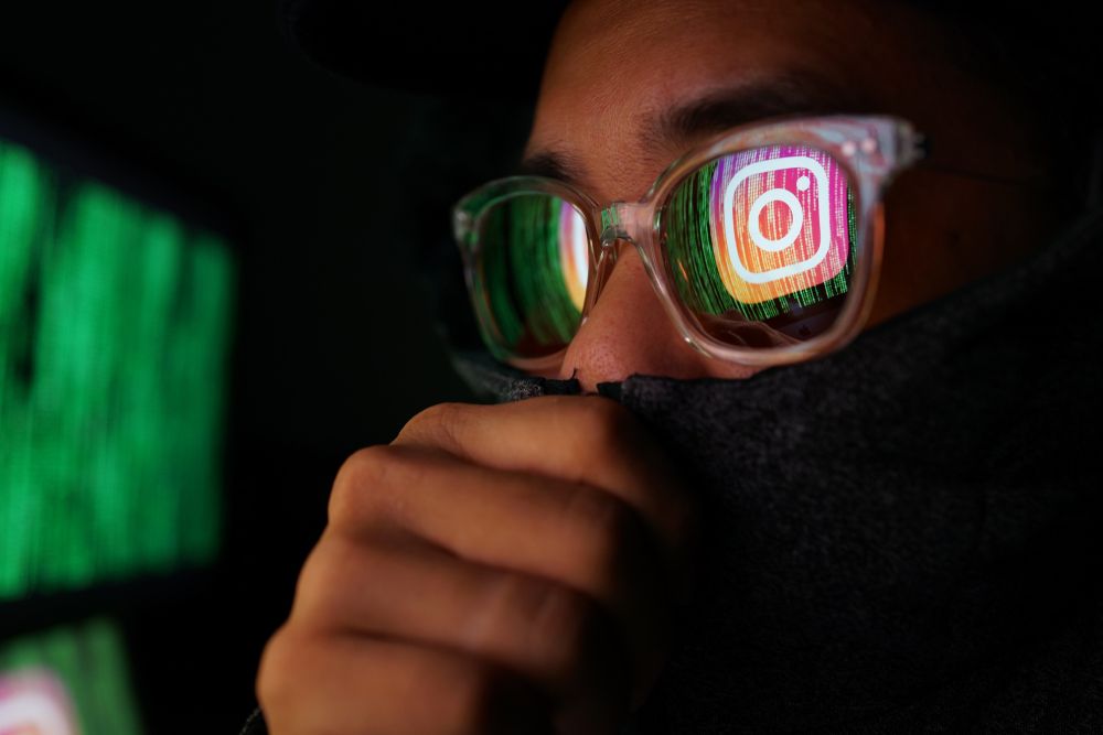 A hacker with Instagram&amp;#039;s logo reflected in his glasses 