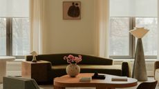 A modern living room with a warm spring color palette. Two big windows are facing the street with blinds and curtains on them.