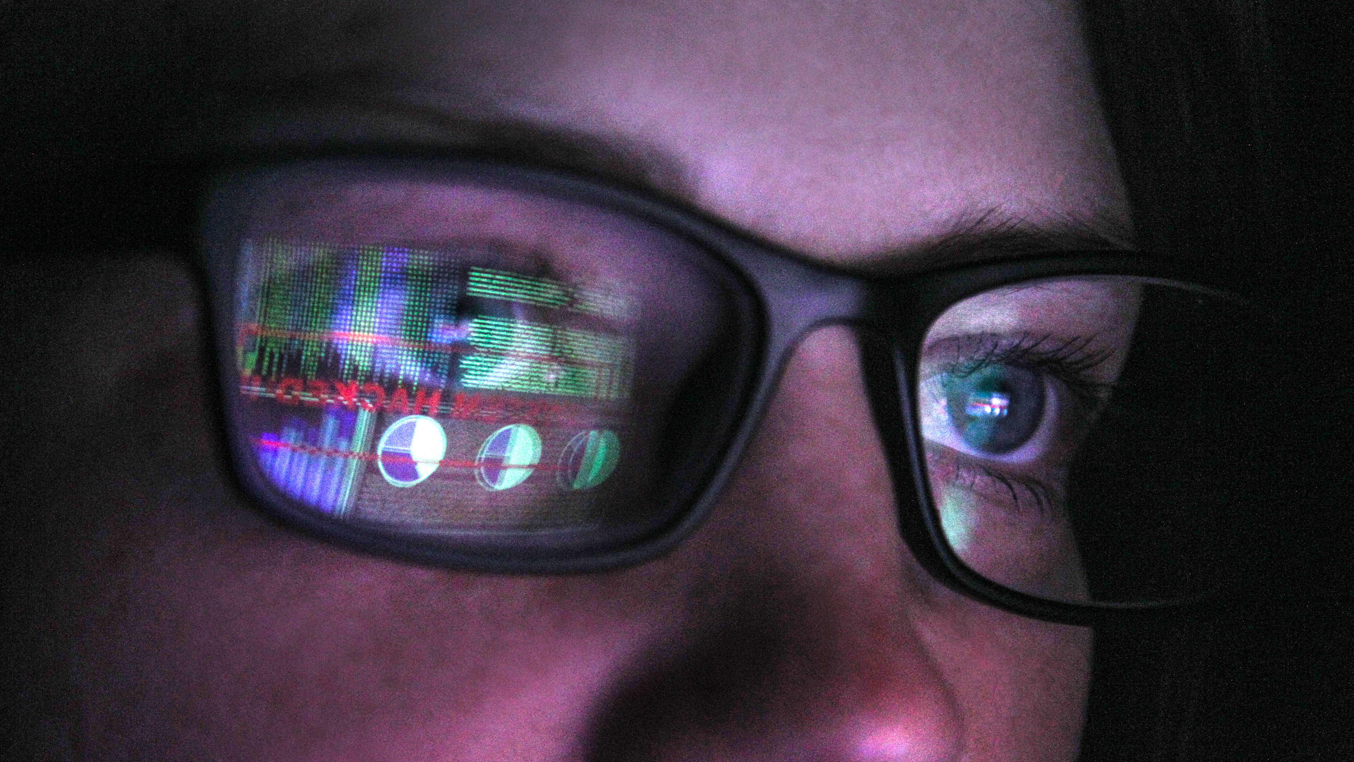 A woman wearing glasses with the reflection of a computer screen showing graphs in one of the lenses