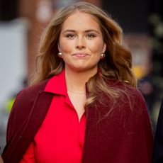 Princess Catharina-Amalia smiling in a red dress and burgundy cape