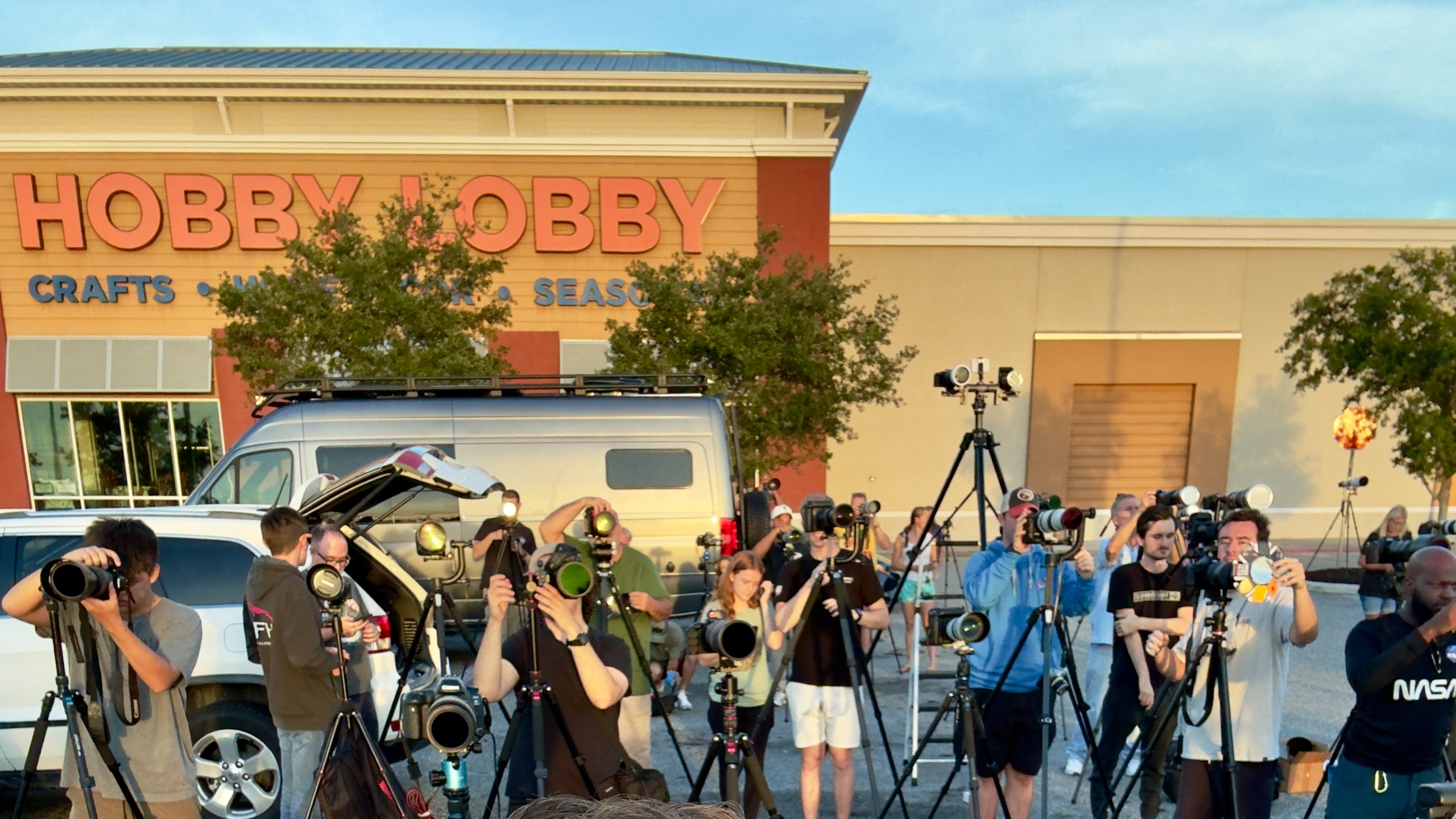 A group of photographers stand in the parking lot of a Hobby Lobby.