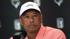 Tiger Woods wearing a salmon polo and white cap during a press conference