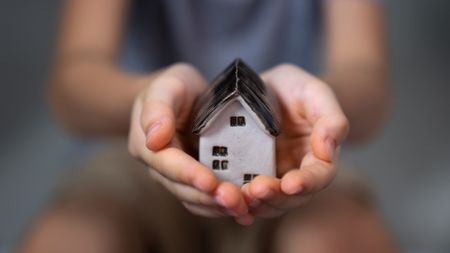 A person holds a small ceramic house in their hands