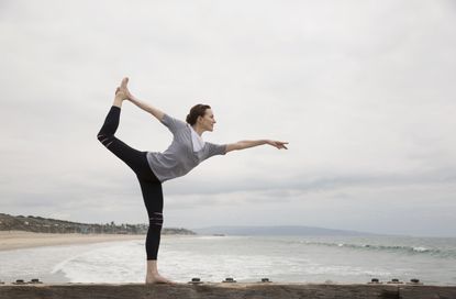 Woman doing yoga king dancer pose on beach