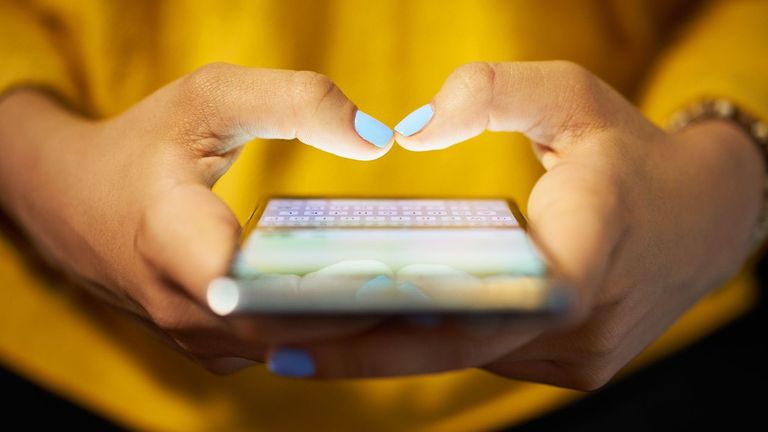 Lady with turquoise nails wearing a mustard sweater busy on a mobile phone