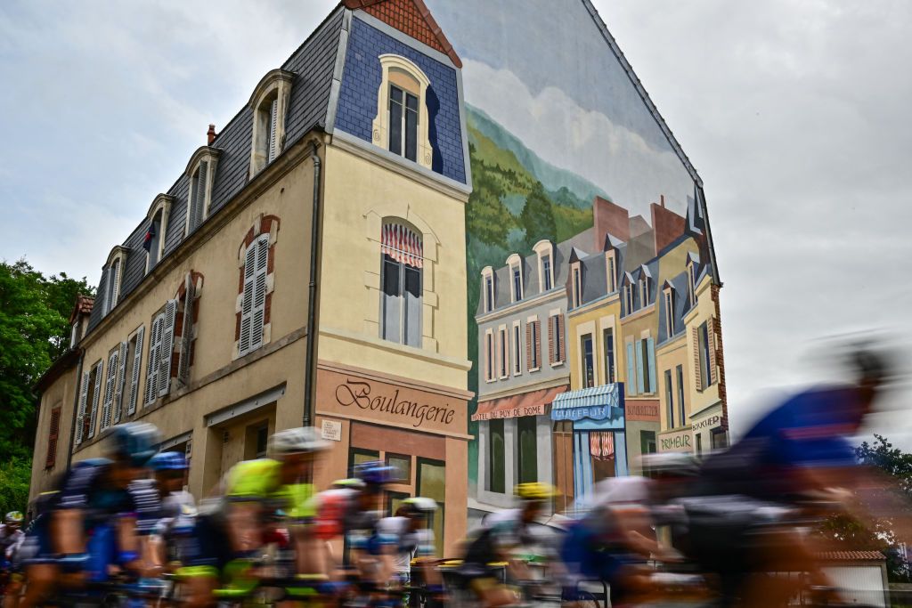 The pack of riders cycles past a mural painted on the side of a building during the 11th stage of the 110th edition of the Tour de France cycling race, 180 km between Clermont-Ferrand and Moulins, in central France, on July 12, 2023. (Photo by Marco BERTORELLO / AFP)