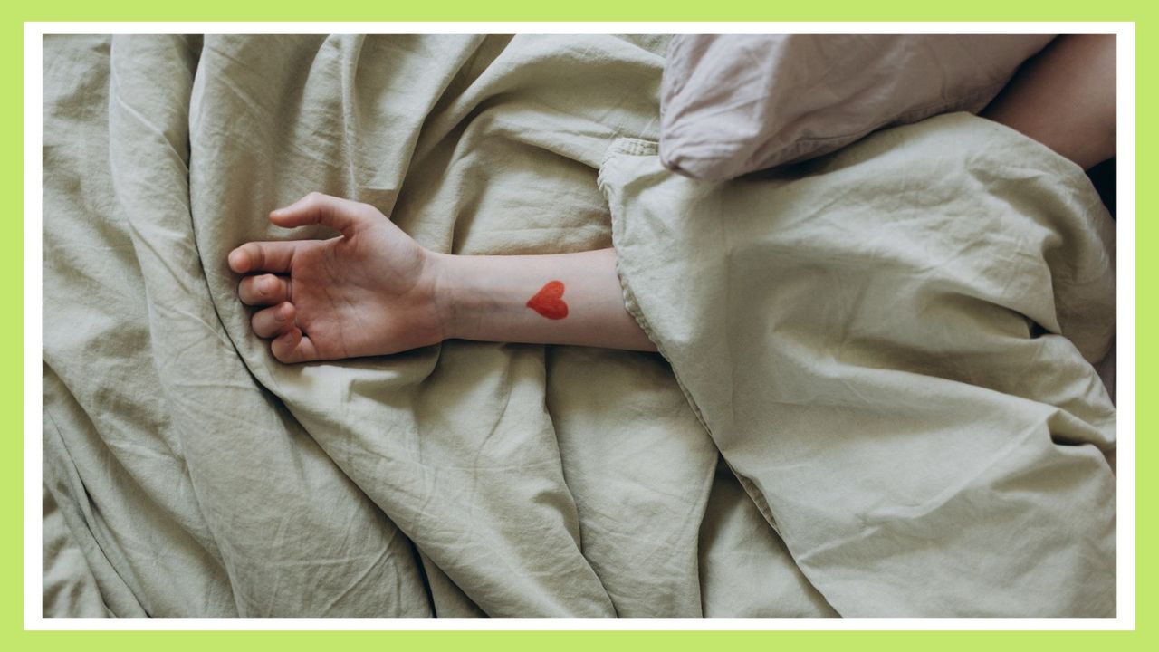 woman&#039;s arm laid out across the bed and sheets with a red tattoo on her wrist—one of the best cute tattoo ideas