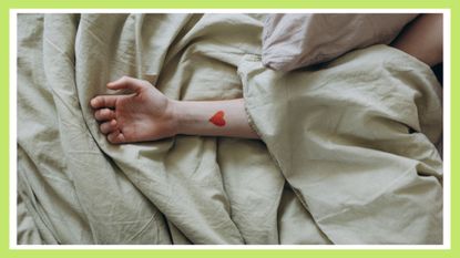 woman's arm laid out across the bed and sheets with a red tattoo on her wrist—one of the best cute tattoo ideas