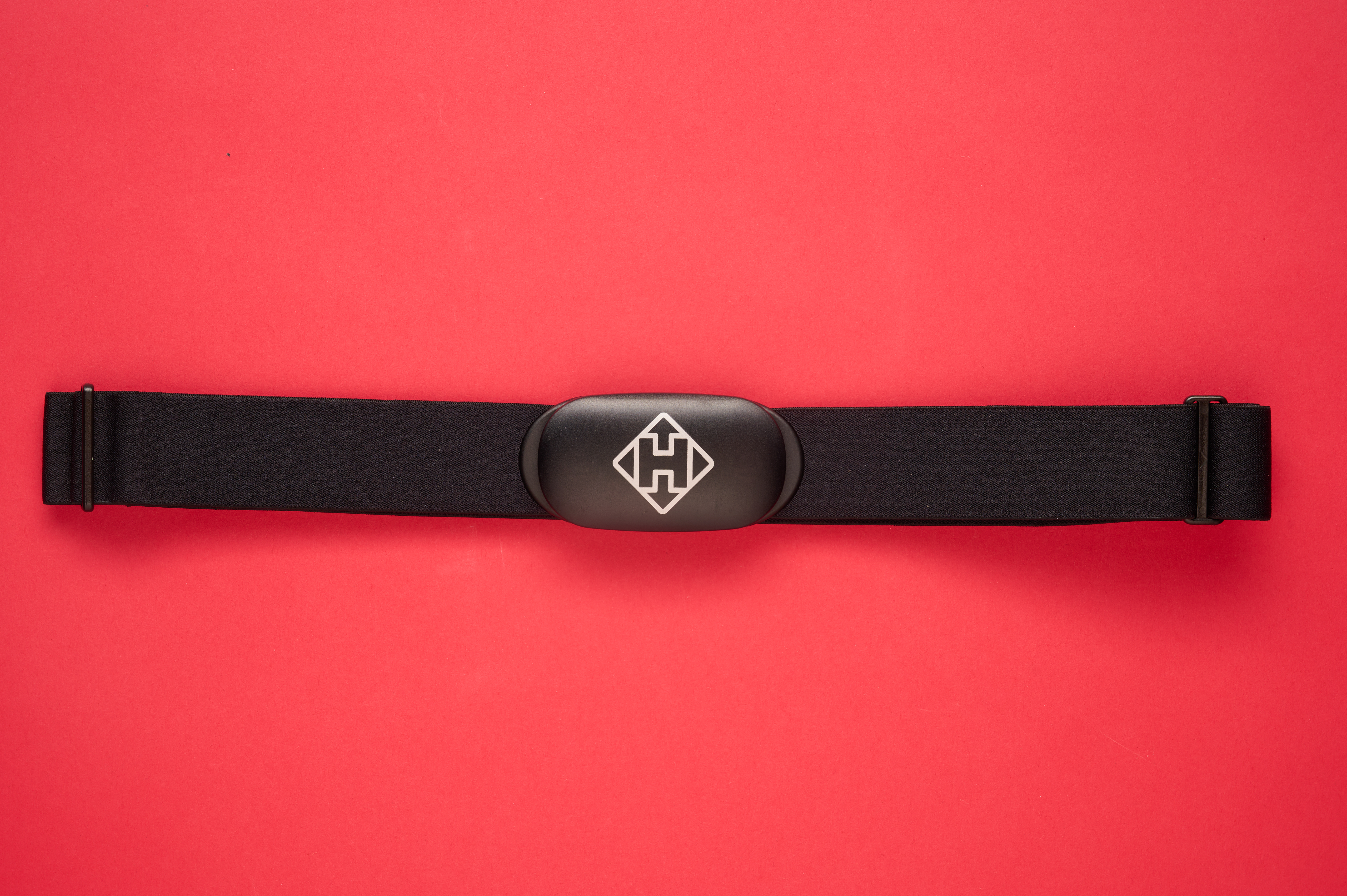 Hammerhead heart rate monitor with its pill like shaped body laid flat on a red background