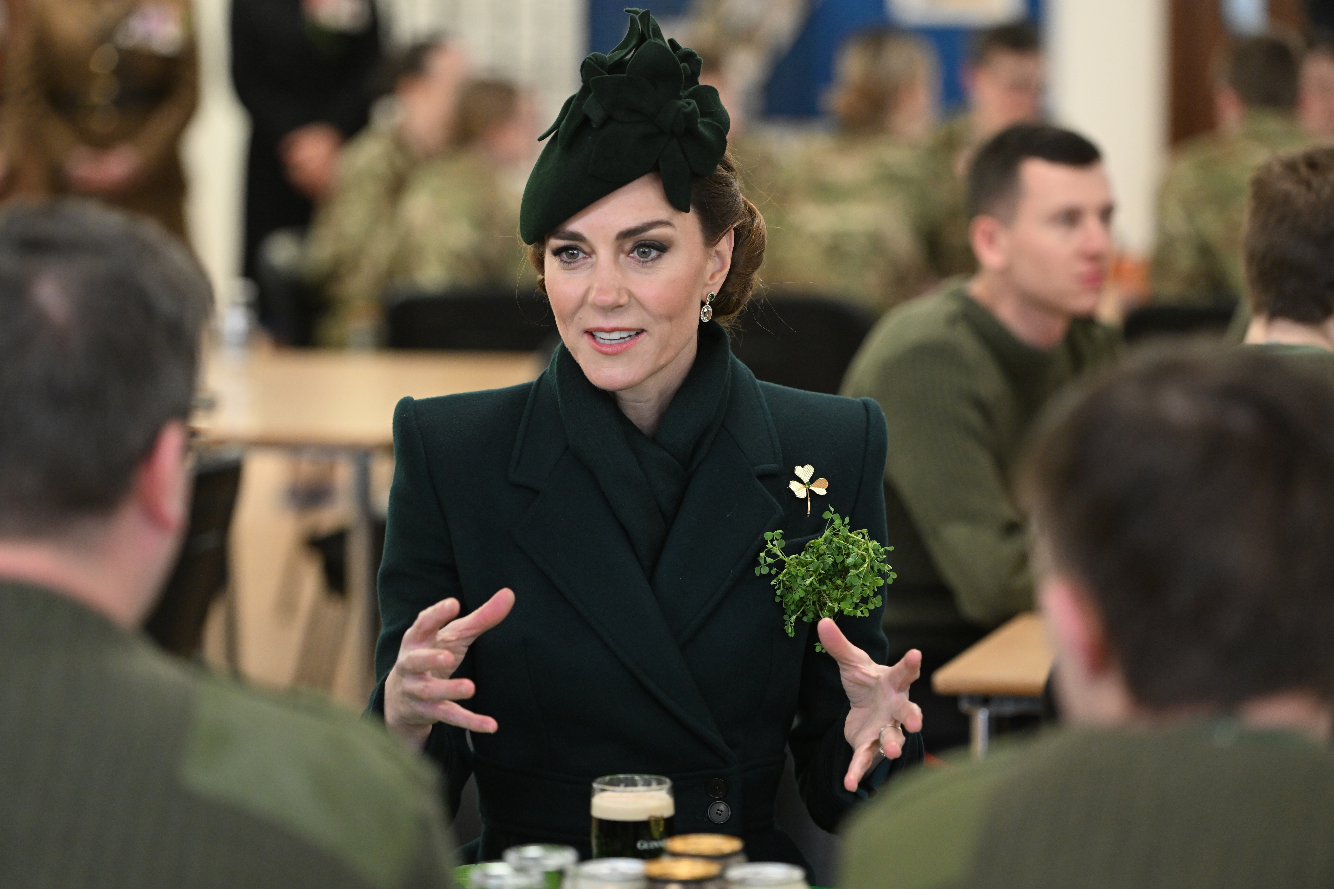 Kate Middleton wearing a green coat sitting at a table with Irish Guards soldiers on St Patrick's Day 2025