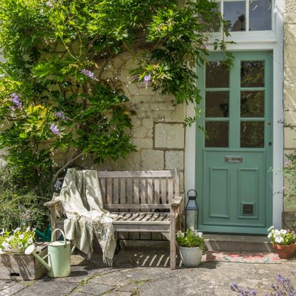 A green front door surrounded by wisteria with a wooden garden bench next to it