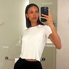 female fashion influencer Tylynn Nguyen poses for a mirror selfie wearing a chic minimalistic outfit with a cropped white tee, multiple hoop earrings, and black pants