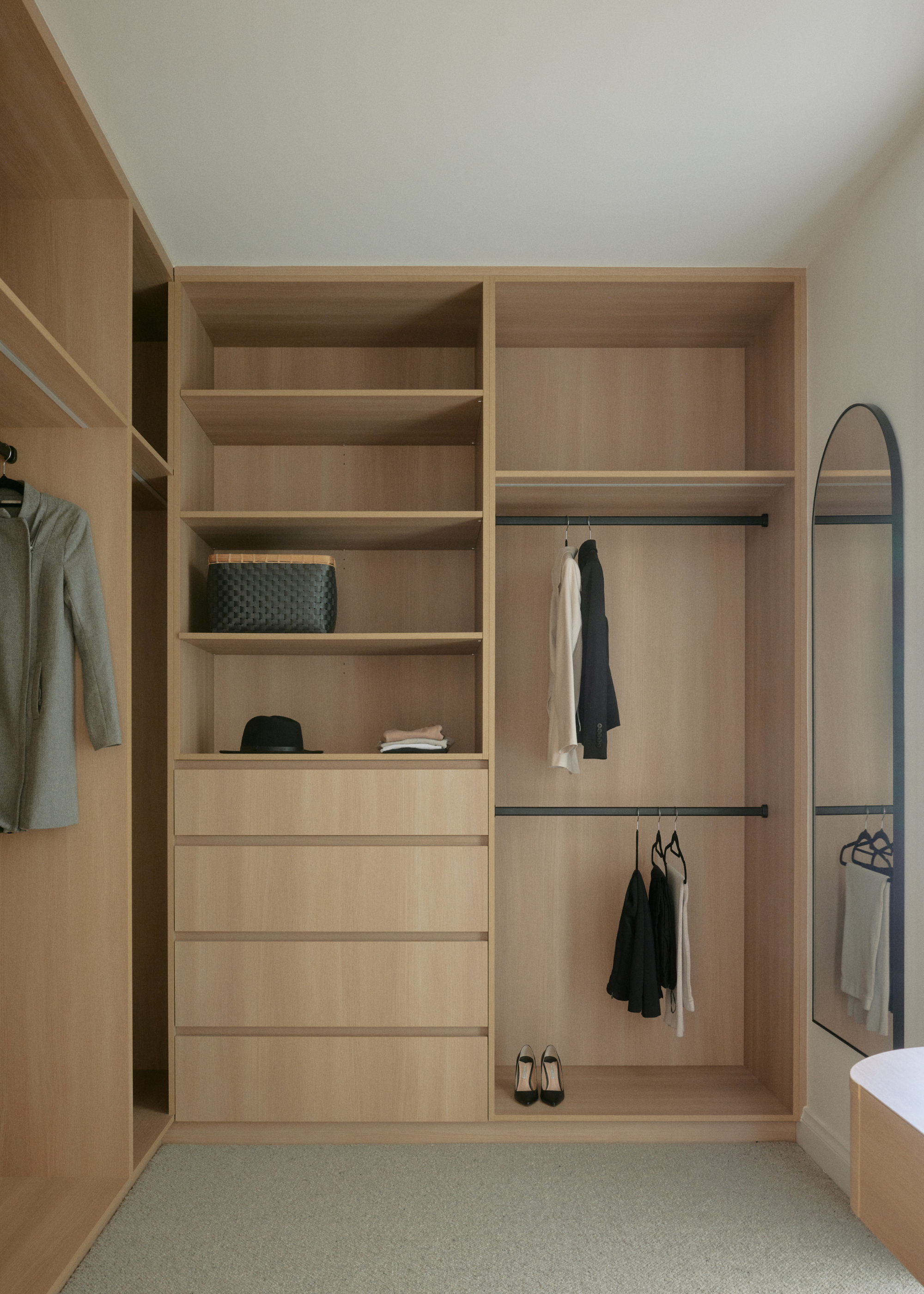 A wood wardrobe with open shelving, hanging clothes and storage drawers alongside a long wall mirror