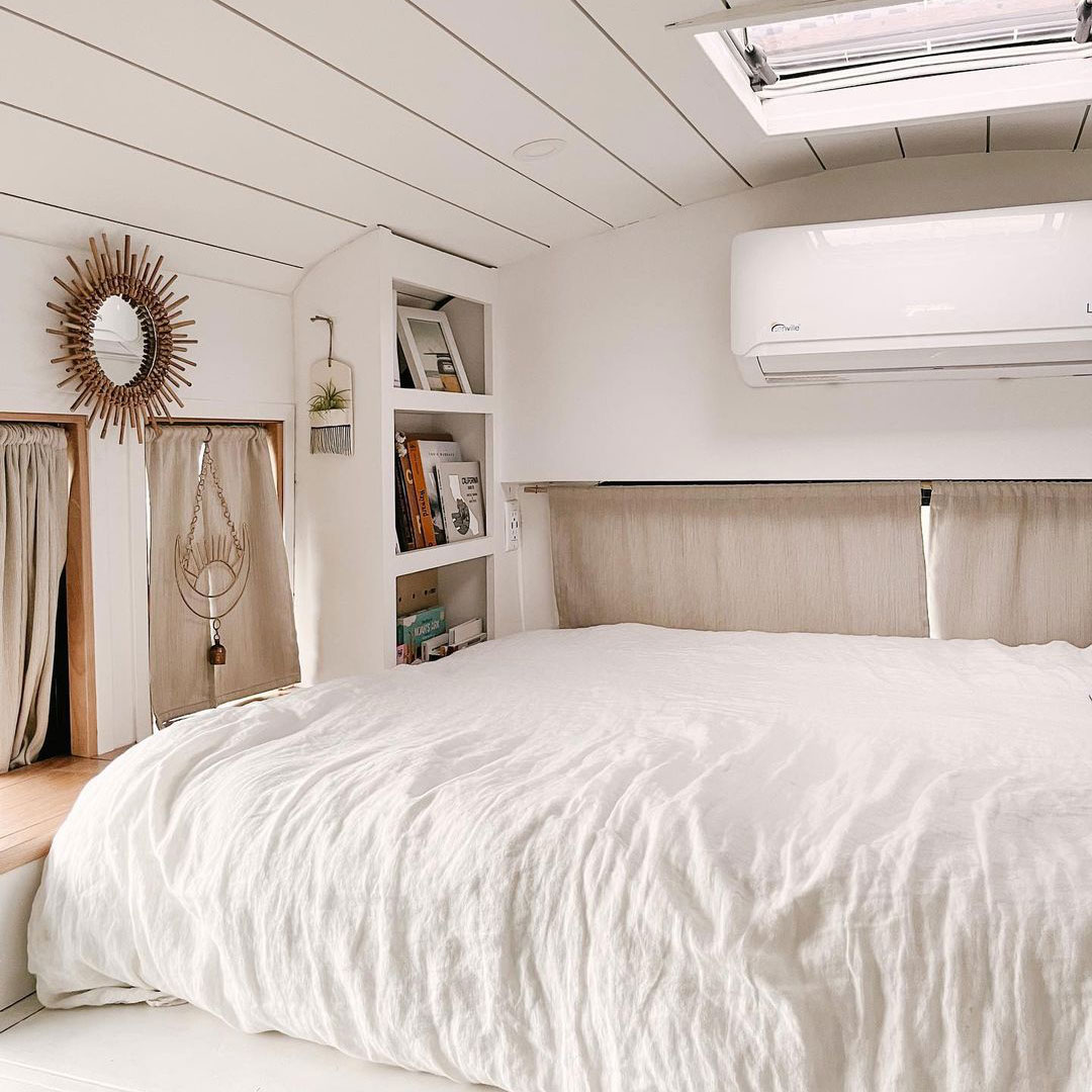 Bedroom space in van with white sheets, shelving and discreet storage