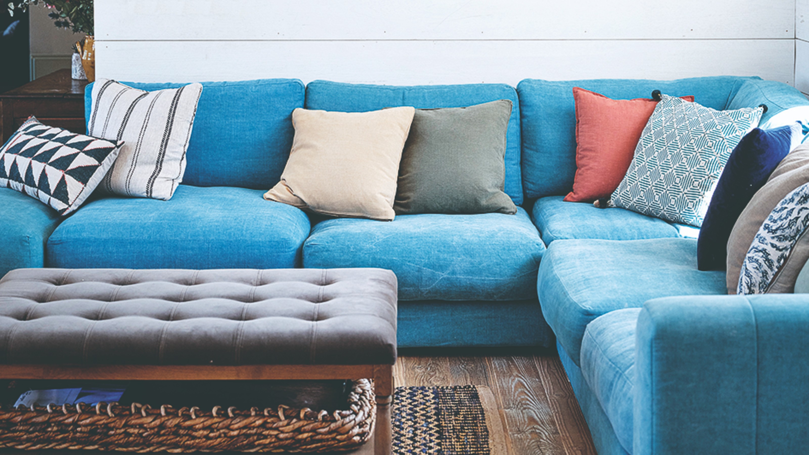 A living room with white wall panelling and a bright blue corner sofa
