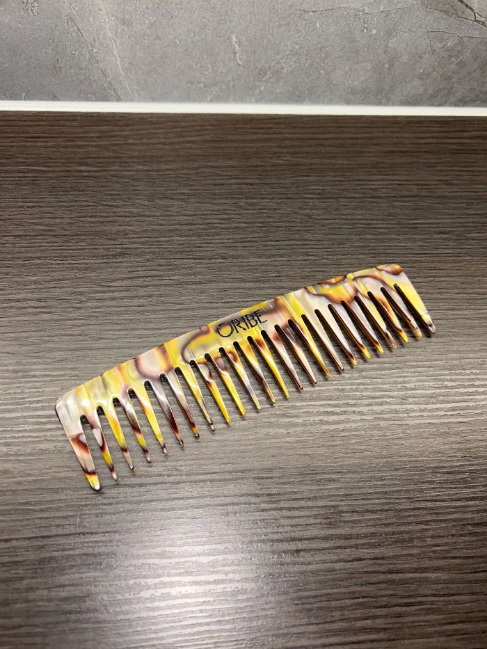 An Oribe comb on the side of a marble bathroom