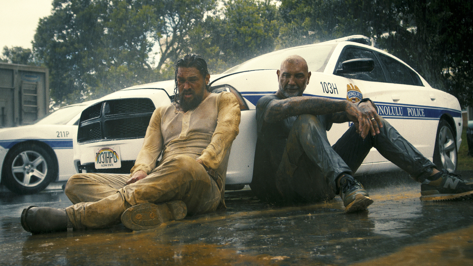 Jonny and James sitting next to a police car in the rain in The Wrecking Crew