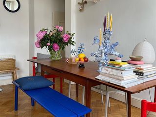 a table with a blue bench red chairs and white bench is pictured with magazines, books, candles, and flowers on top of it